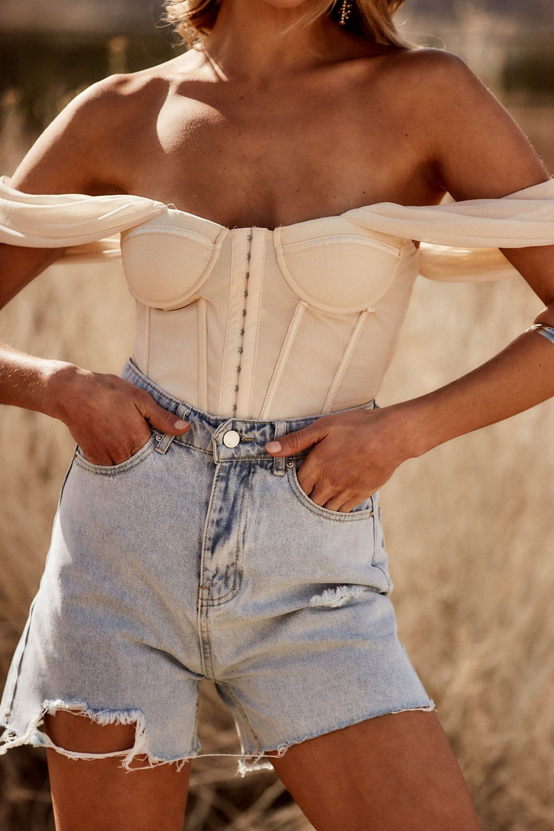 Cream corset top with boned structure and off-the-shoulder sleeves, styled with denim shorts.