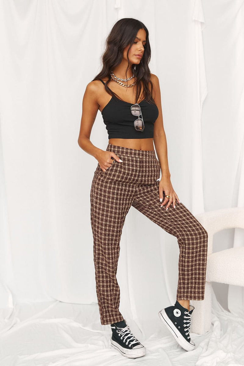 Model wears brown checkered trousers with a black crop top and high-top sneakers.