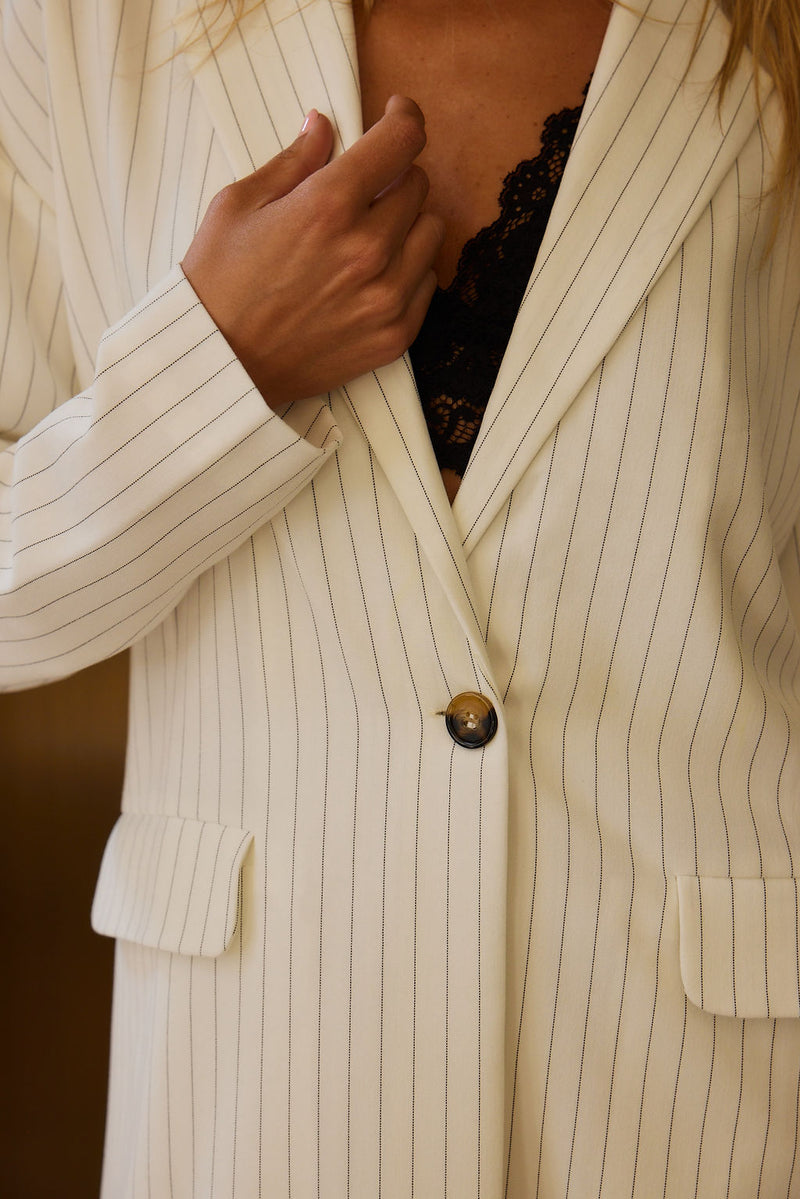 Close-up of cream pinstripe blazer dress with tortoise button and black lace bralette.