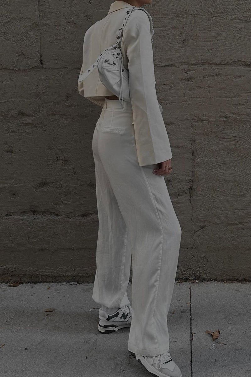 Side view of white wide leg trousers styled with a cropped blazer and sneakers.