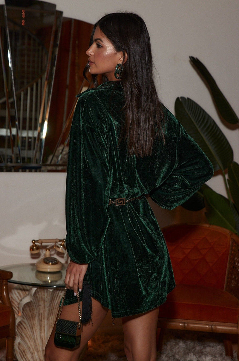 Full-length view of the emerald mini dress showing the drape and movement.
