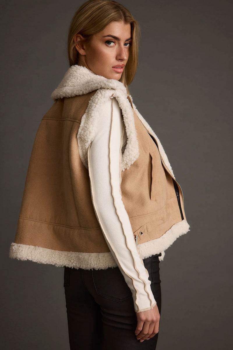 Side view of a beige suede vest with cream sherpa lining and collar, worn over an ivory top.