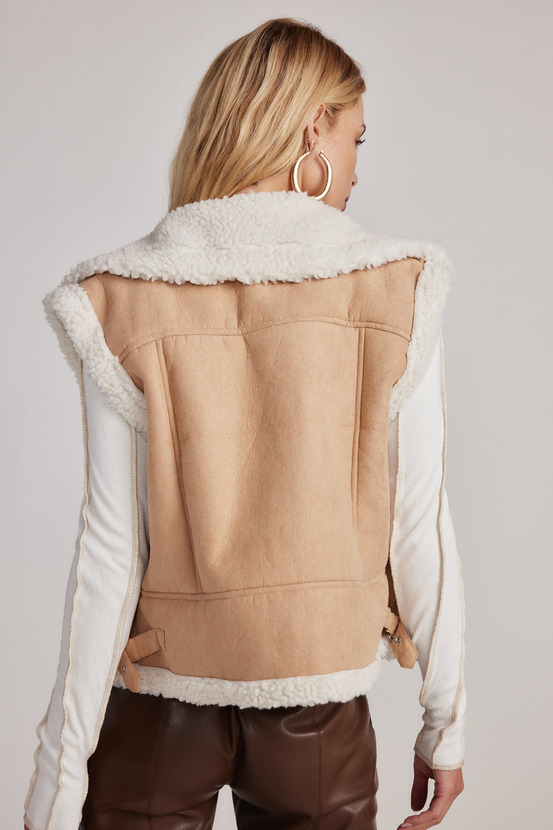 Back view of beige faux suede sherpa-lined vest with cream fur trim and buckle tabs.