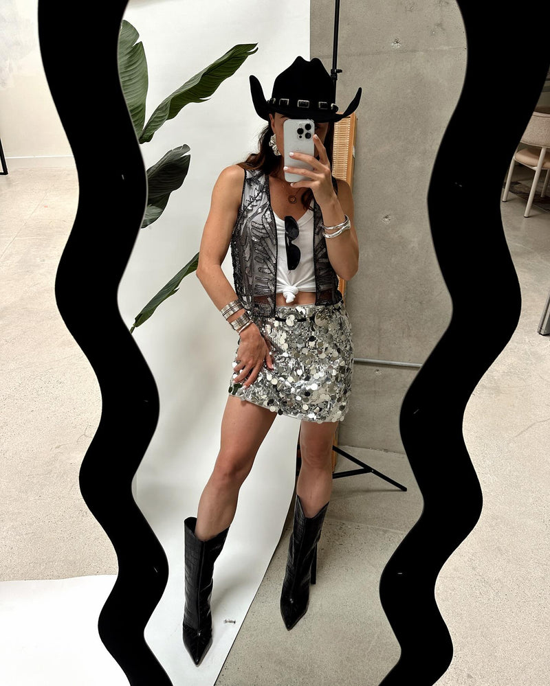 Silver disco sequin mini skirt styled with cowboy hat, vest, and black boots for a festival look.
