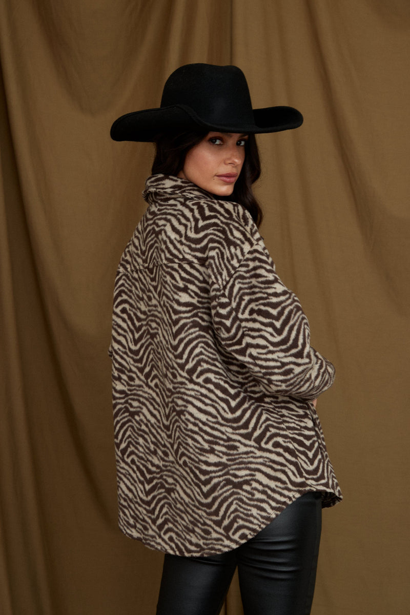 Brown zebra print shacket shown from the back with a black wide-brim hat.